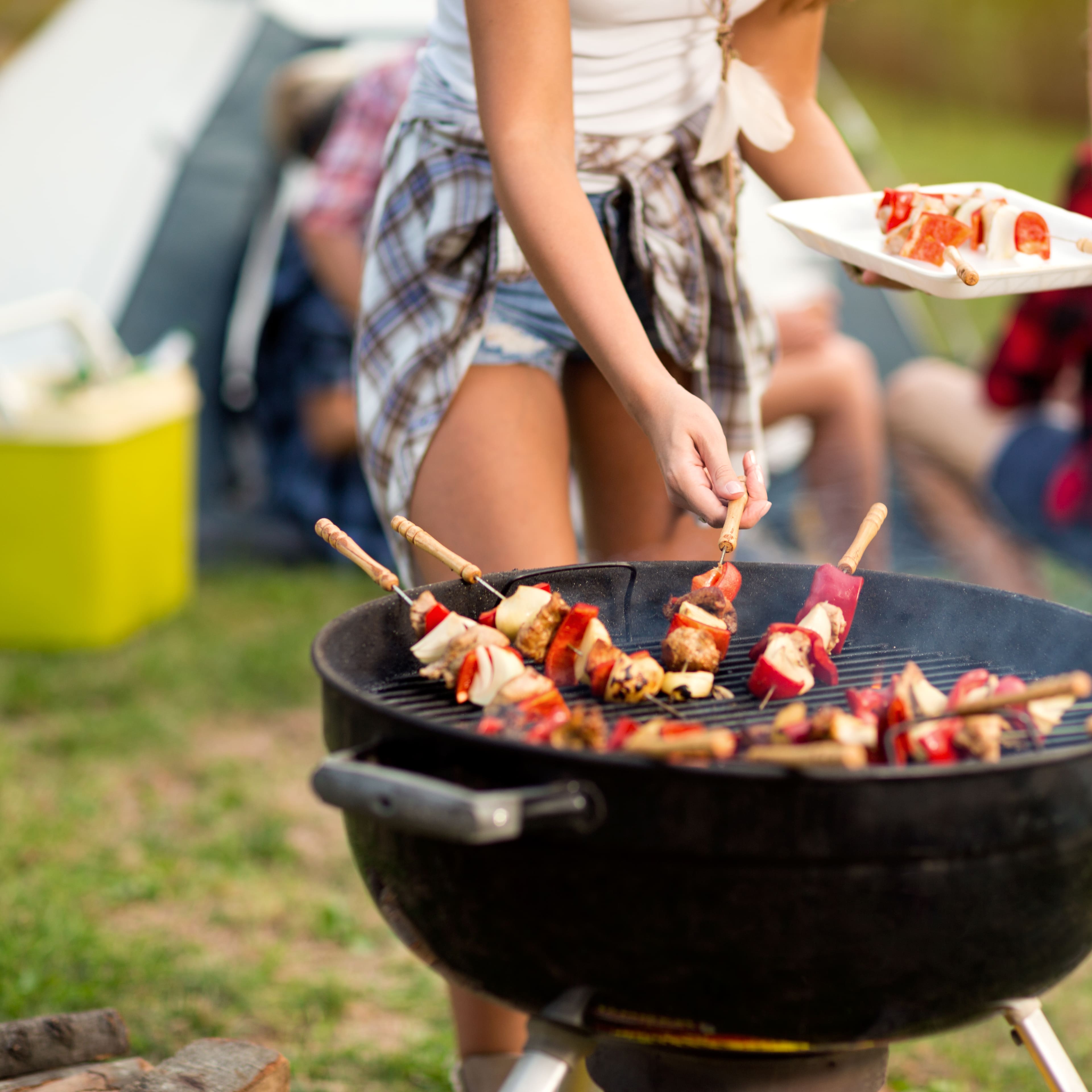 Frau steht auf dem Zeltplatz an einem Grill