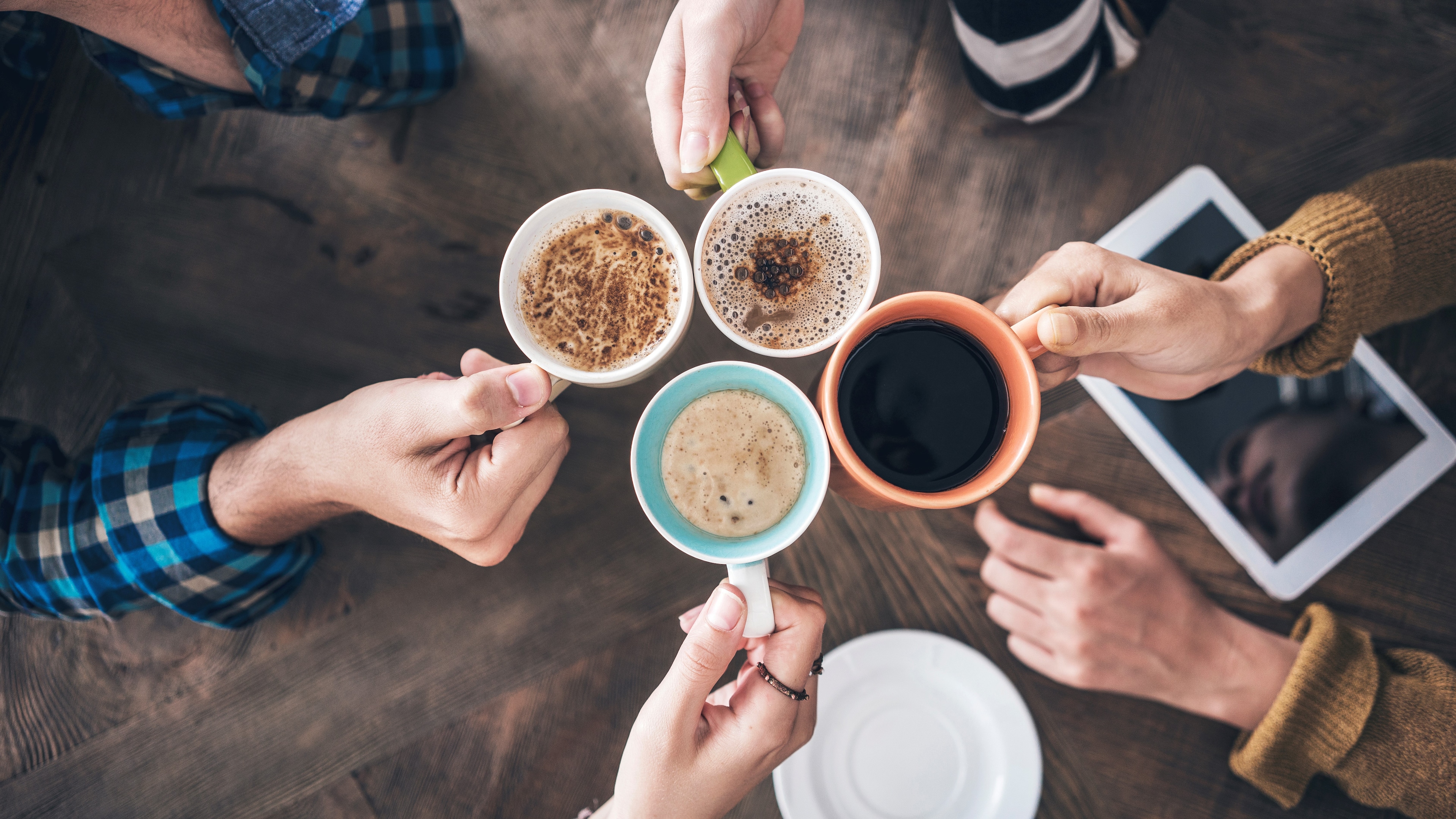 4 Menschen stoßen mit Kaffee über Bürotisch an.