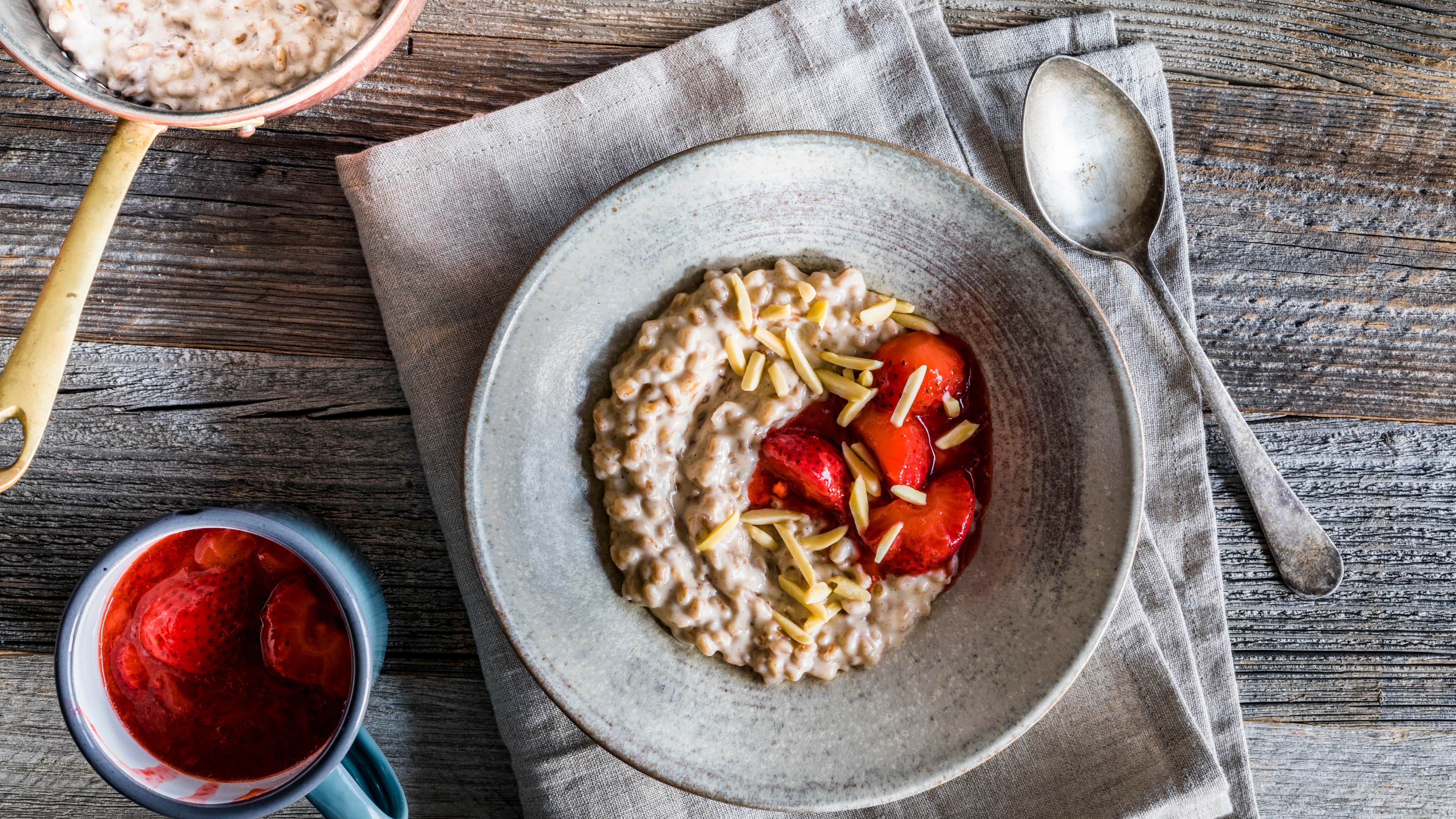 Rezept für Dinkel-Milchreis mit Erdbeerkompott Ein tiefer Teller mit cremigem Brei, getoppt mit Erdbeerkompott, getoppt mit gehobelten Mandeln