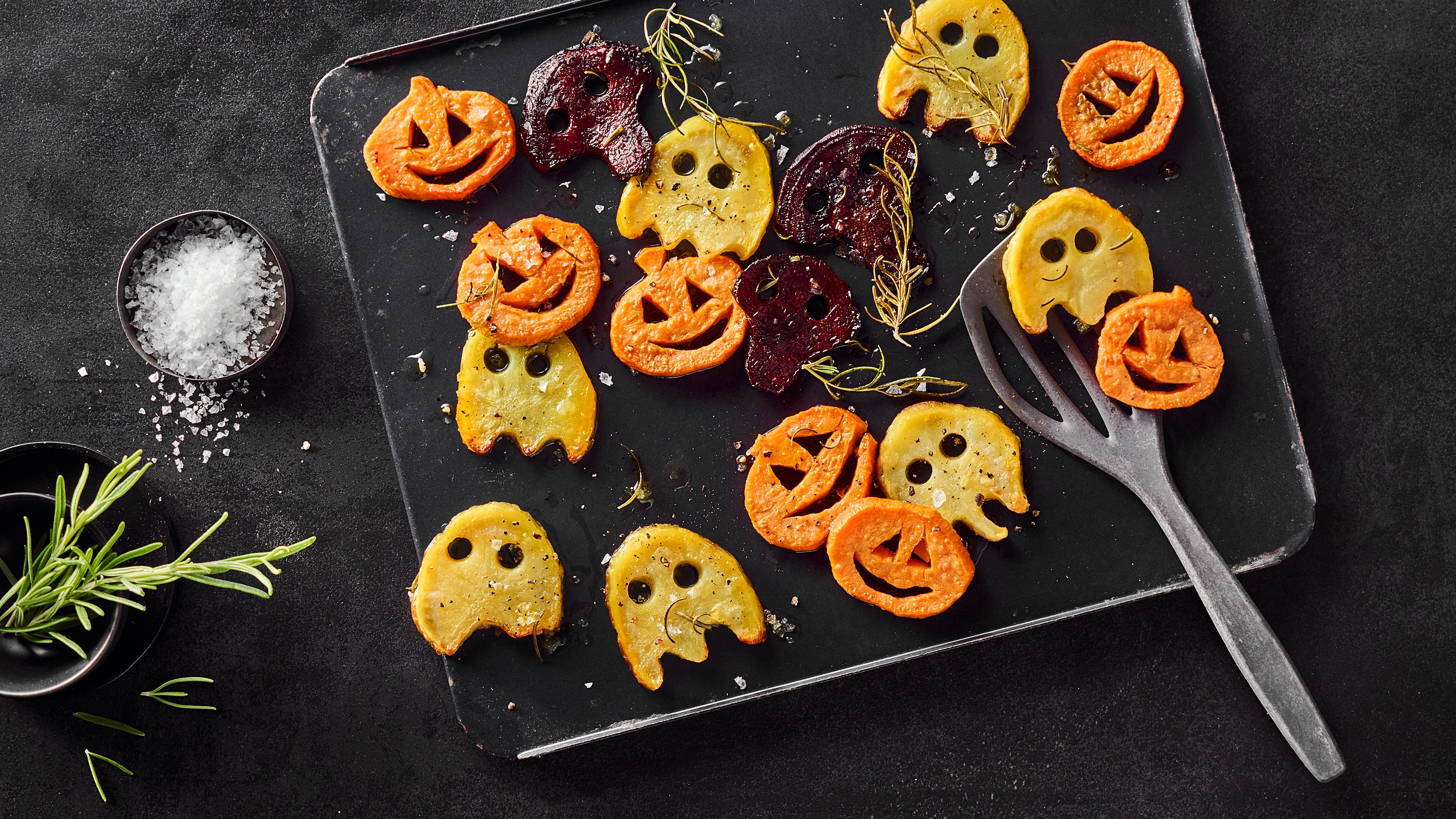 Rezept für Halloween Ofengemüse Eine Platte angerichtet mit Kartoffeln in Geisterform, Kürbissen in Kürbisform sowie Rote Bete in Totenkopfform