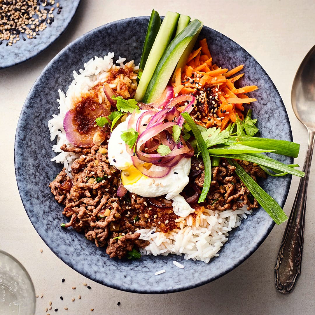 Rezept für Reis Bowl mit Hackfleisch Eine Bowl mit Reis, Hackfleisch, pochierten Eiern, Lauchzwiebeln, Möhren, roten Zwiebel und dunkler Sauce