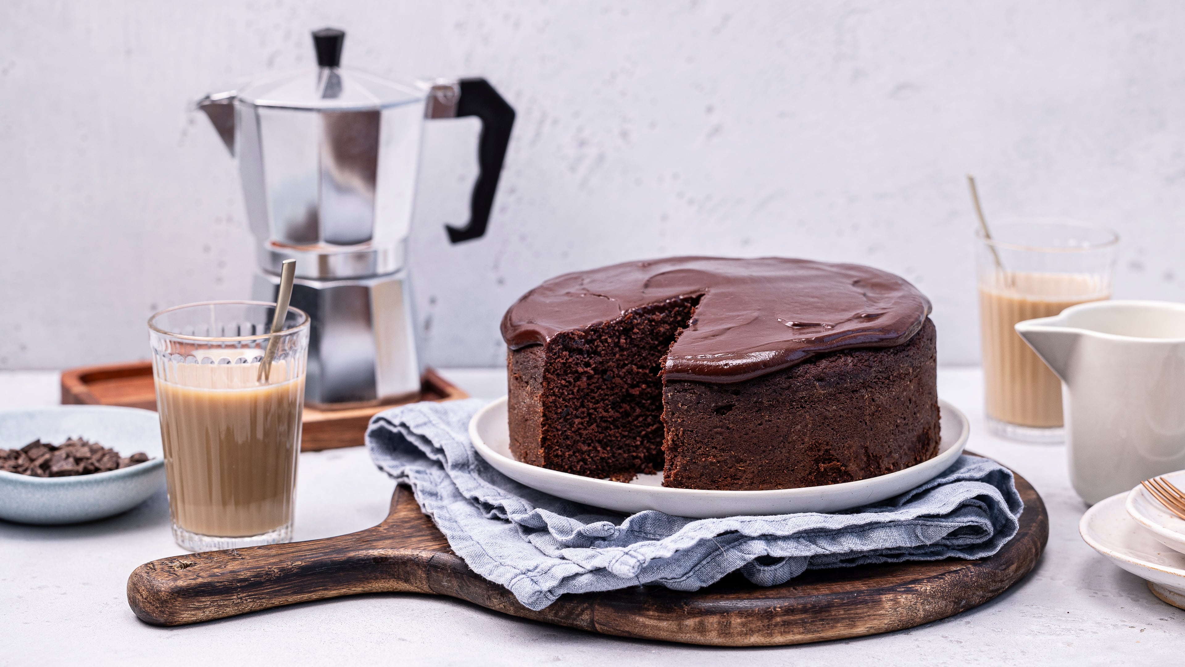 Rezept für einen saftigen Schokokuchen Ein runder, hoher safiger Schokoladenkuchen, getoppt mit einer glänzenden, luftigen Schokoladencreme auf einem runden Teller