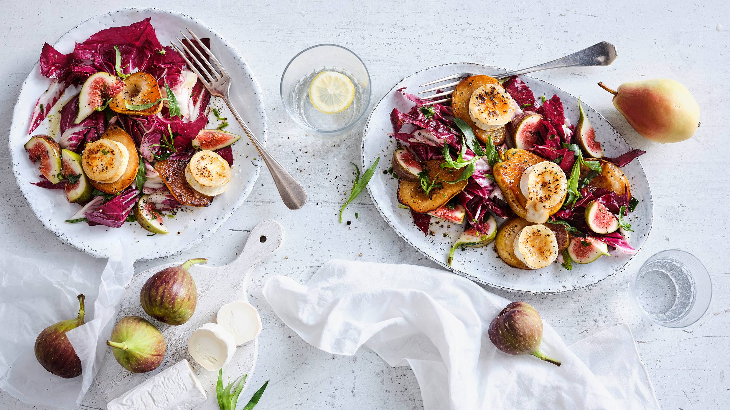 Rezept für überbackene Birne mit Radicchio Ein ovaler Teller mit Birnenhälften mit überbackenem Ziegenkäse, Feigen, Radicchio-Salat und gehacktem Estragon