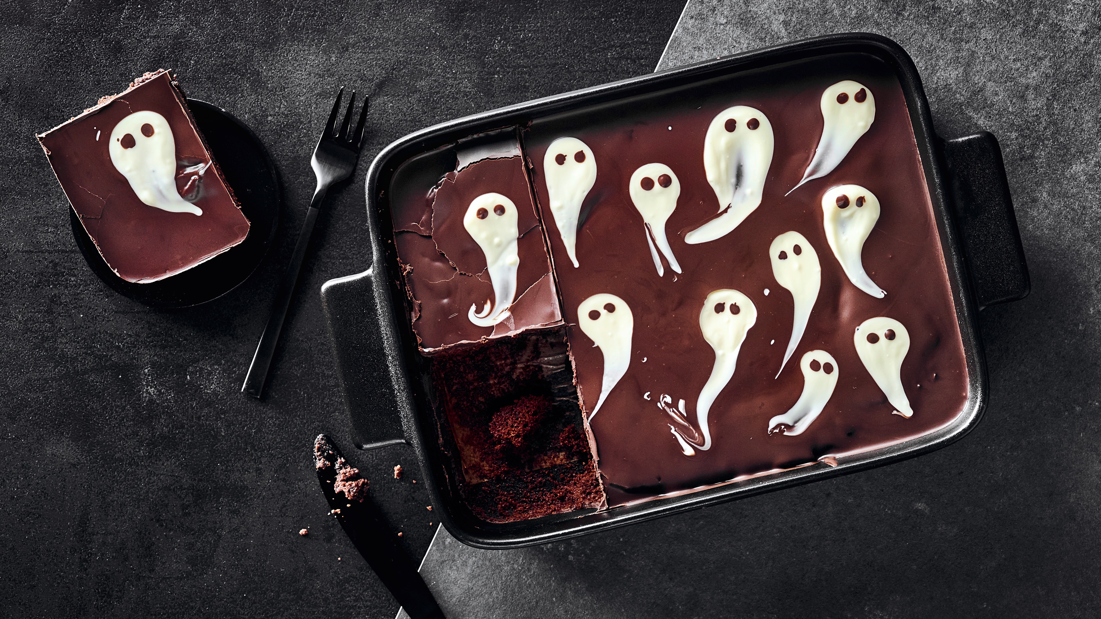 Rezept für Geisterbrownies Eine Keramikform gefüllt mit saftigem Schokoboden, einer dunklen Schokoglasur, verziert mit Geistern aus weißer Schokolade