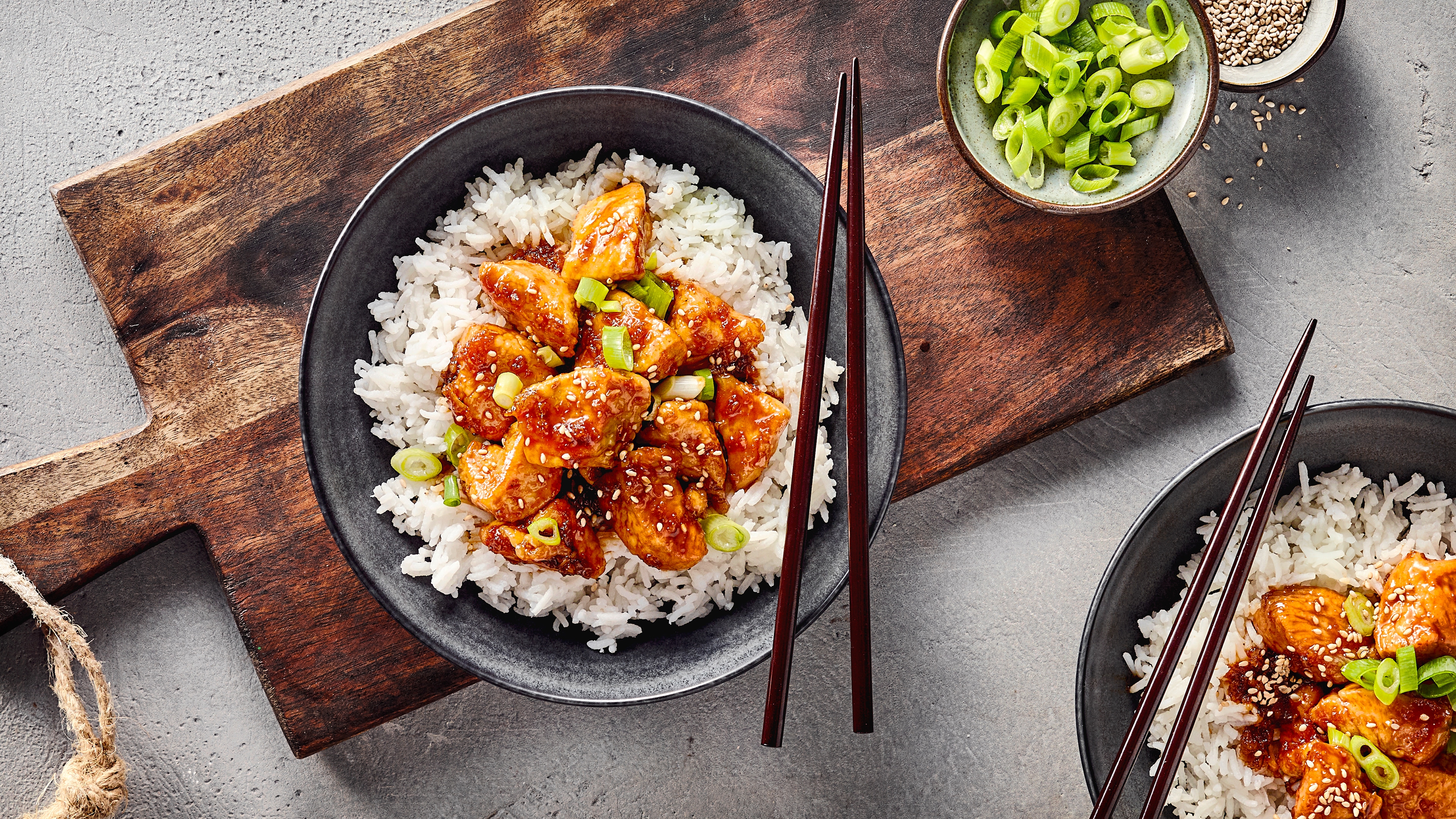Rezept für Honey Garlic Chicken Eine Schüssel mit Reis, getoppt mit glasierten Hähnchenstücken, geschnittenen Frühlingszwiebeln und Sesamsamen