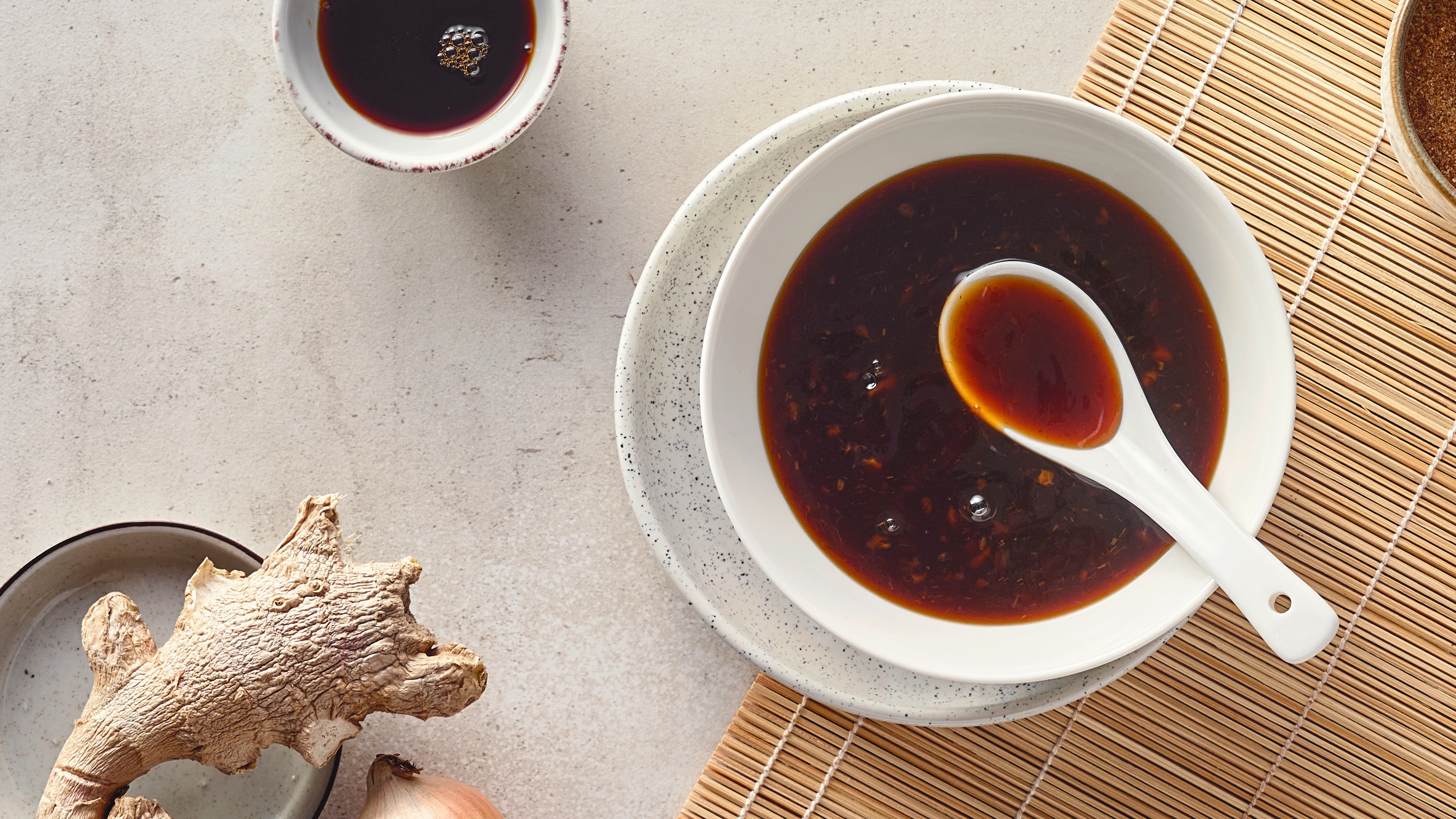 Rezept für selbstgemachte Teriyaki Sauce Eine Schale mit dunkelbrauner, dickflüssiger Soße mit sichtbaren Gewürzen, darin liegt ein weißer Keramiklöffel