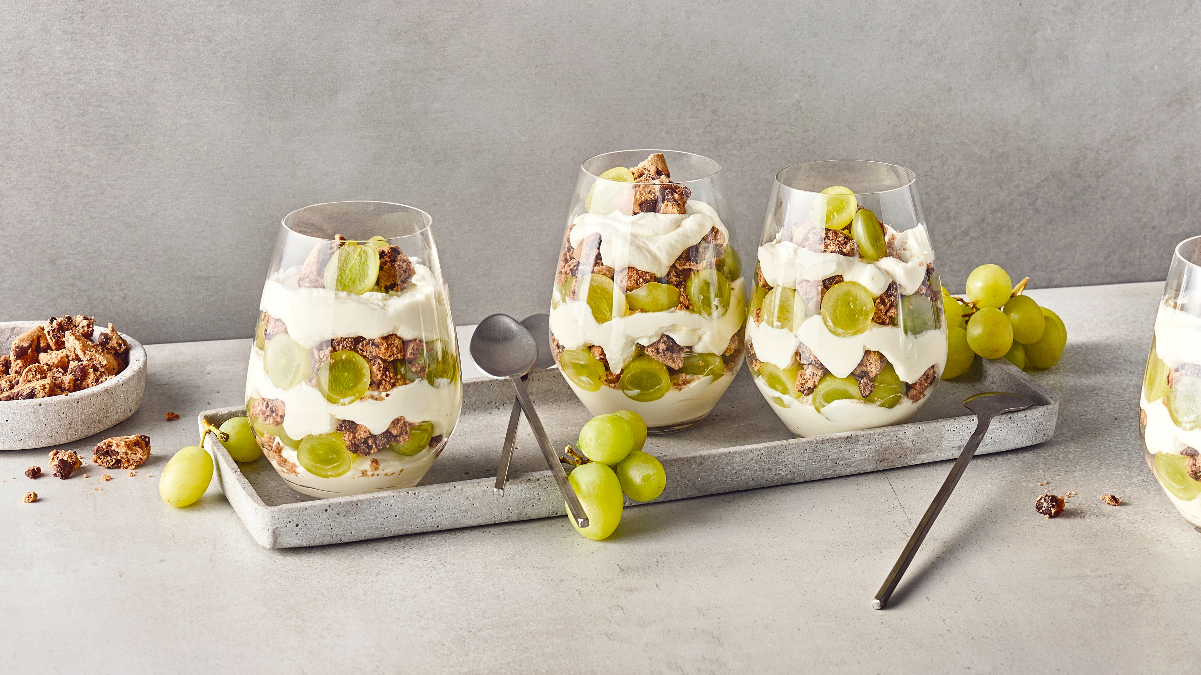 Rezept für Weintrauben-Dessert mit Cookies Dessertgläser, gefüllt mit Schichten aus heller Creme, grünen Weintrauben und gebröselten Keksen mit Schokostückchen